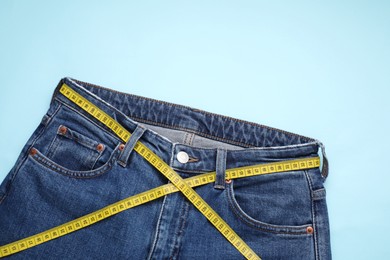 Photo of Jeans and measuring tape on light blue background, top view. Space for text