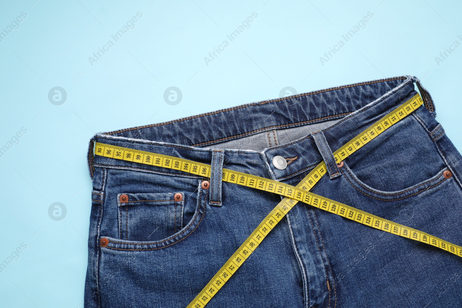 Photo of Jeans and measuring tape on light blue background, top view. Space for text