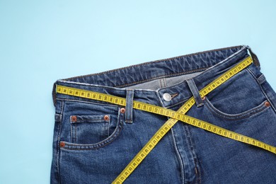 Photo of Jeans and measuring tape on light blue background, top view. Space for text