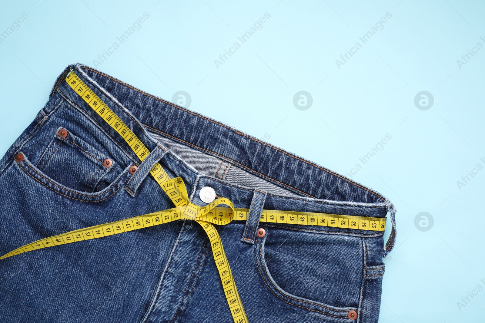 Photo of Jeans and measuring tape on light blue background, top view. Space for text