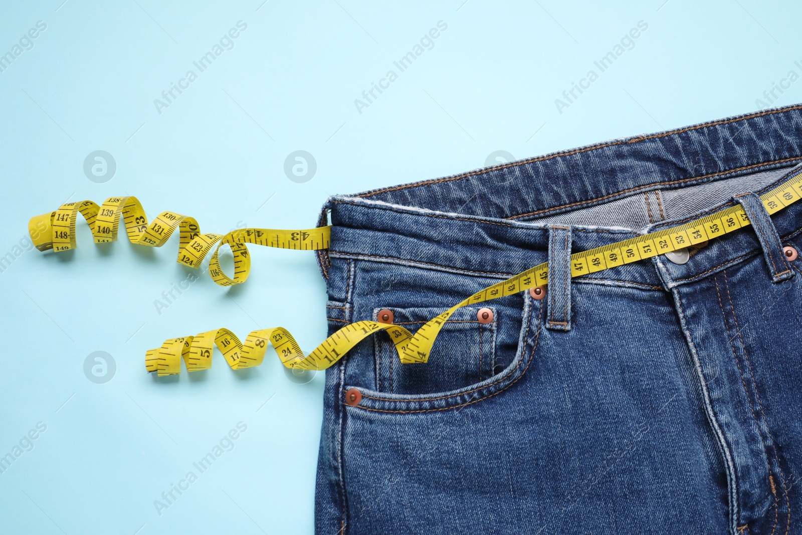 Photo of Jeans and measuring tape on light blue background, top view