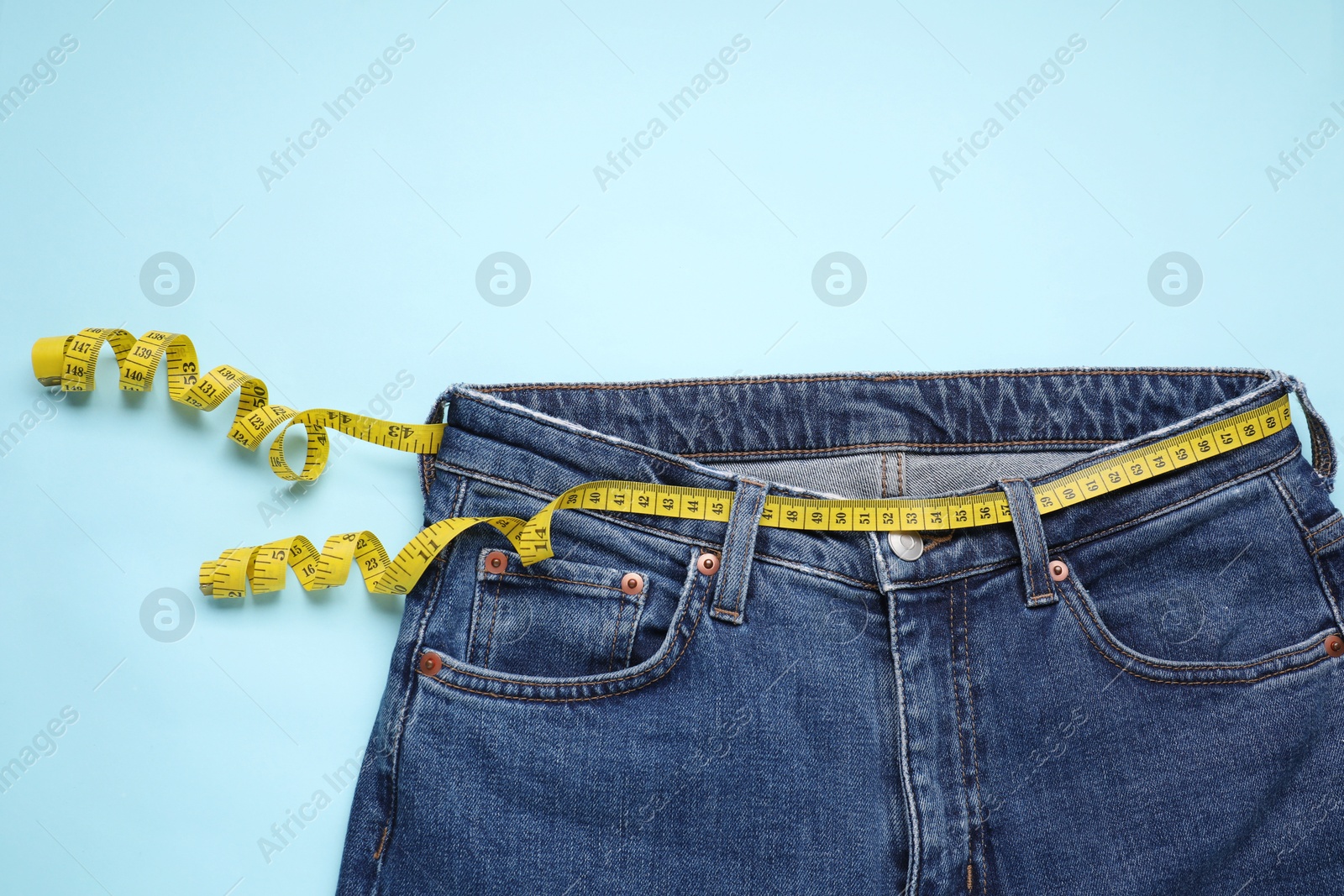 Photo of Jeans and measuring tape on light blue background, top view. Space for text