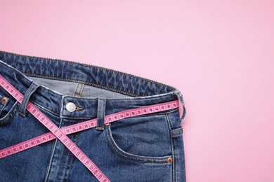 Photo of Jeans and measuring tape on pink background, top view. Space for text