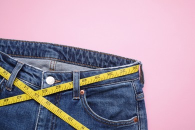 Photo of Jeans and measuring tape on pink background, top view