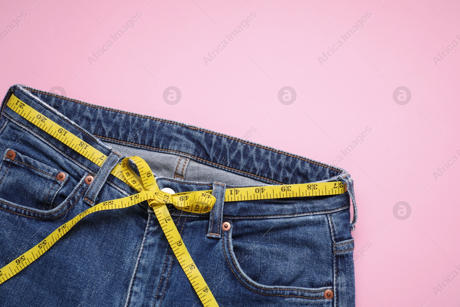 Photo of Jeans and measuring tape on pink background, top view. Space for text