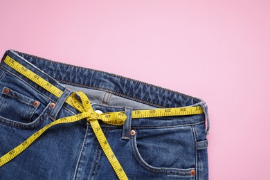 Photo of Jeans and measuring tape on pink background, top view. Space for text