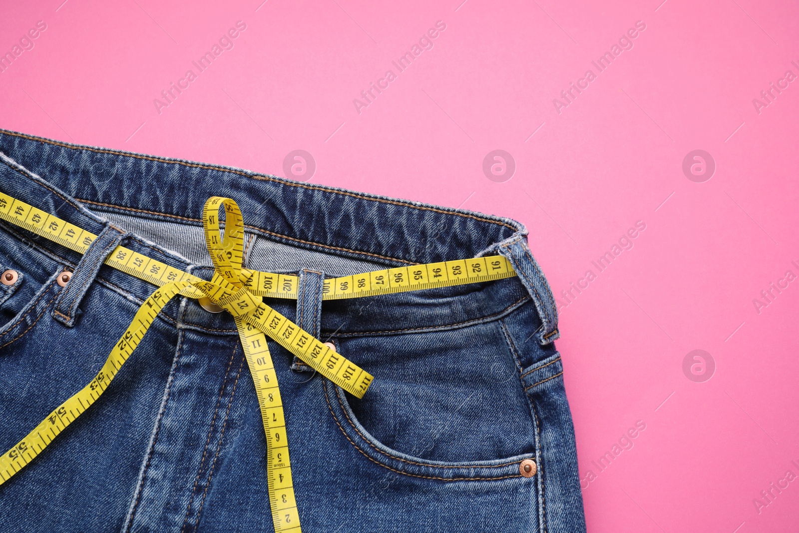 Photo of Jeans and measuring tape on pink background, top view. Space for text