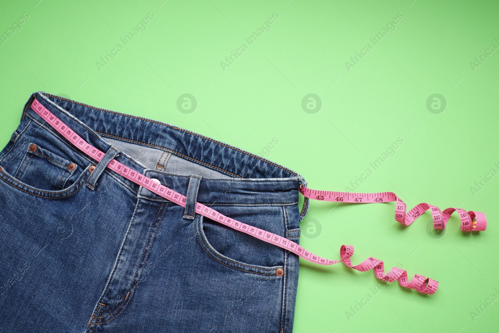 Photo of Jeans and measuring tape on light green background, top view. Space for text