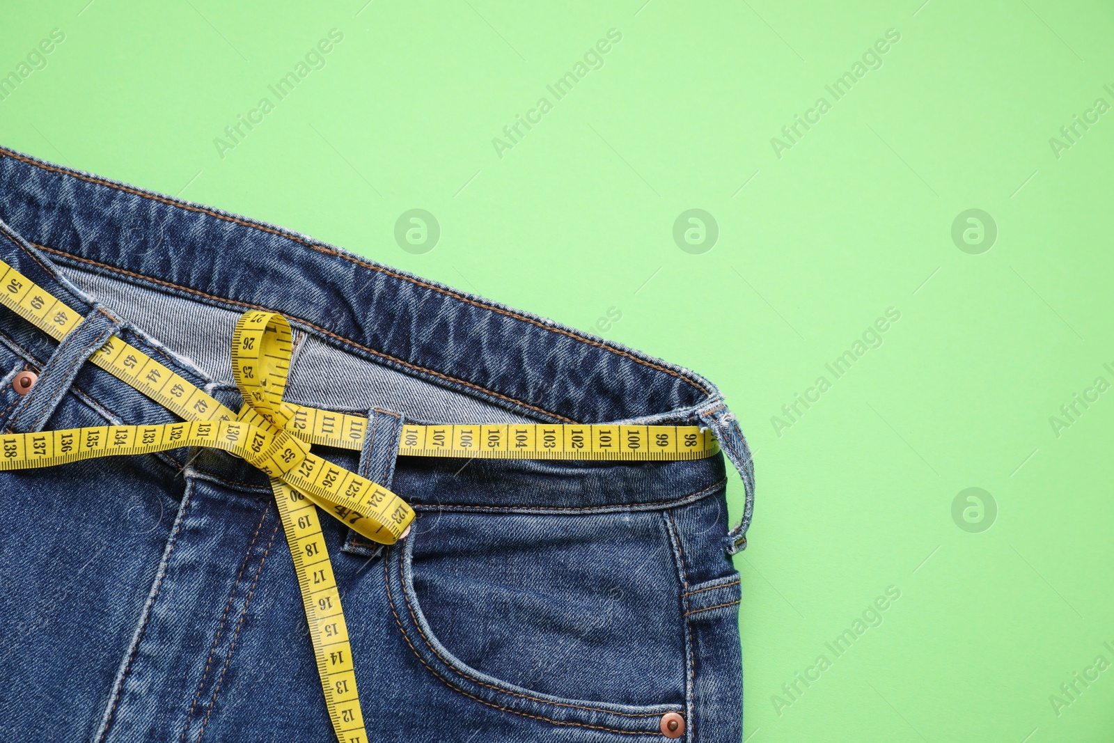 Photo of Jeans and measuring tape on light green background, top view. Space for text