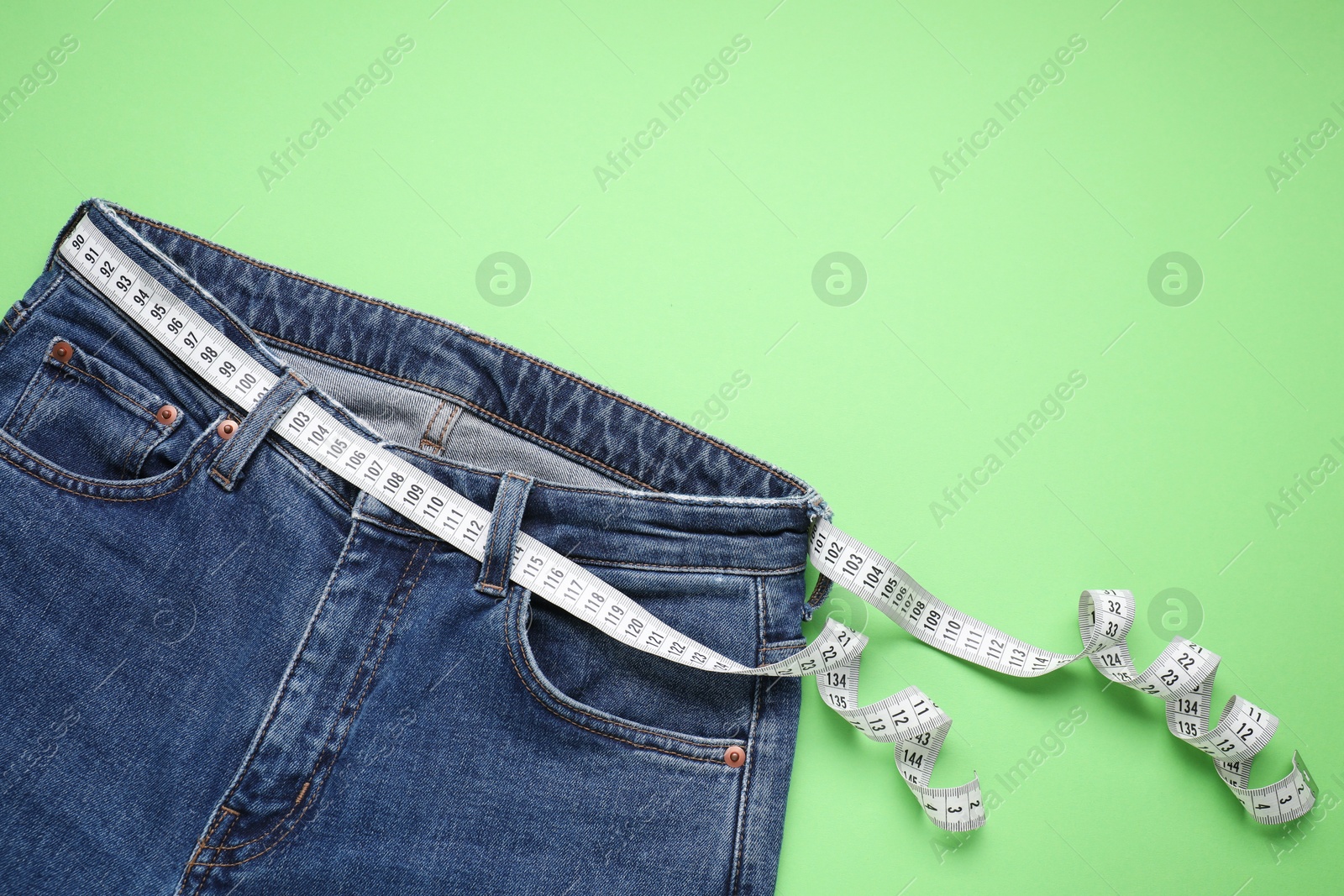 Photo of Jeans and measuring tape on light green background, top view. Space for text