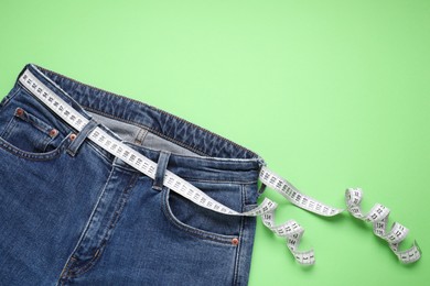 Photo of Jeans and measuring tape on light green background, top view. Space for text