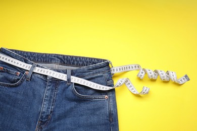 Photo of Jeans and measuring tape on yellow background, top view. Space for text