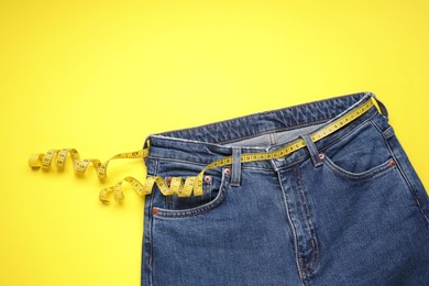 Photo of Jeans and measuring tape on yellow background, top view. Space for text