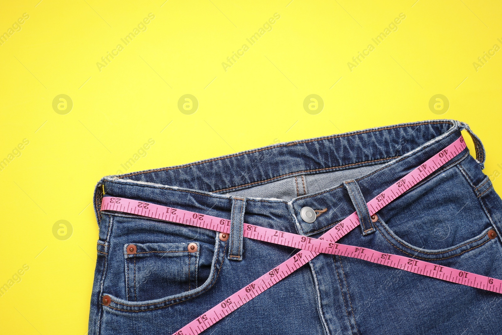 Photo of Jeans and measuring tape on yellow background, top view. Space for text