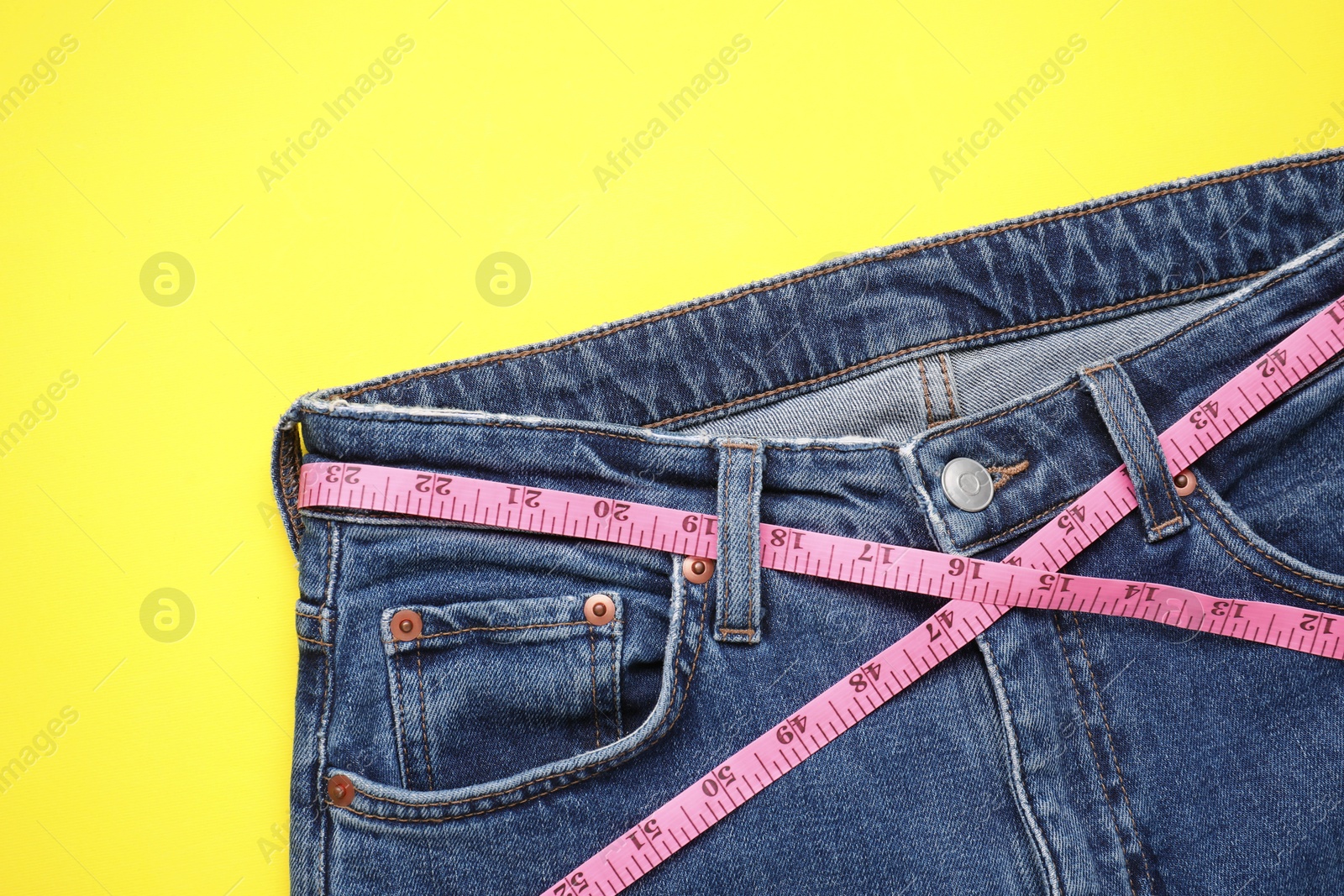 Photo of Jeans and measuring tape on yellow background, top view