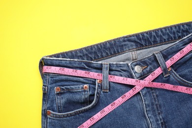 Photo of Jeans and measuring tape on yellow background, top view