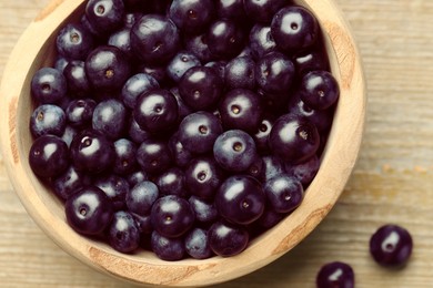 Ripe acai berries in bowl on wooden table, top view