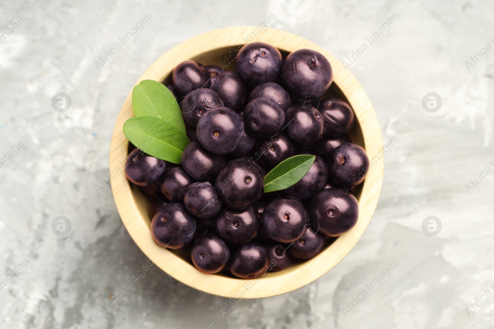 Photo of Ripe acai berries and leaves in bowl on grey textured table, top view