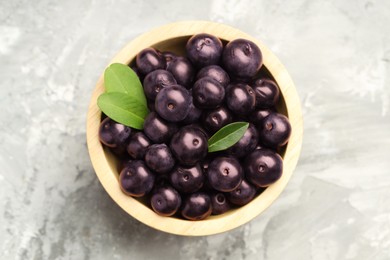 Ripe acai berries and leaves in bowl on grey textured table, top view