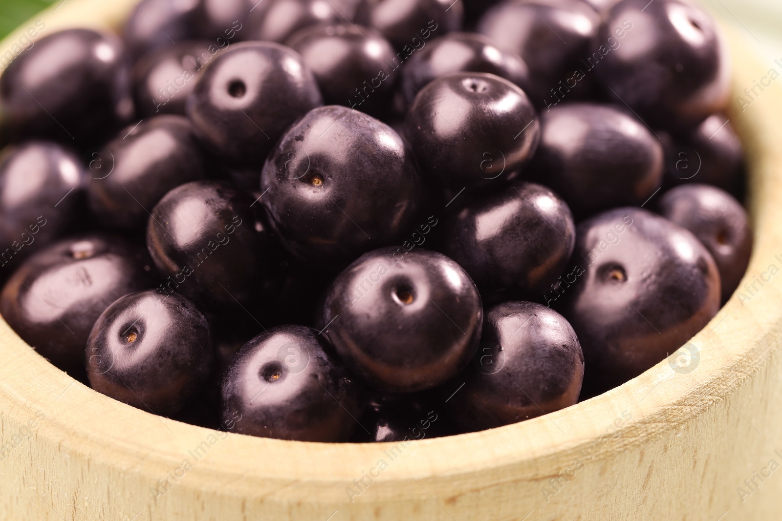 Photo of Ripe acai berries in wooden bowl, closeup