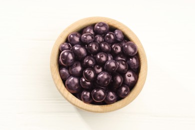 Photo of Ripe acai berries in bowl on white wooden table, top view