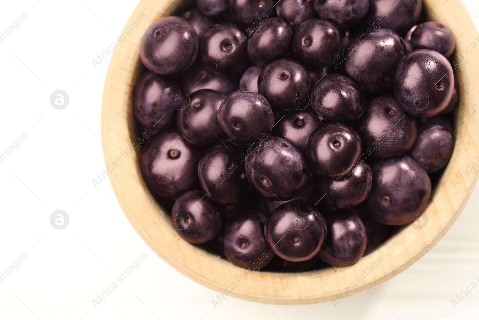 Photo of Ripe acai berries in bowl on white wooden table, top view