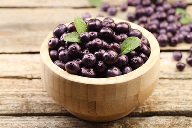 Photo of Ripe acai berries and leaves in bowl on wooden table, closeup