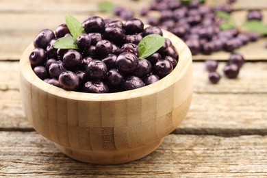 Ripe acai berries and leaves in bowl on table, closeup