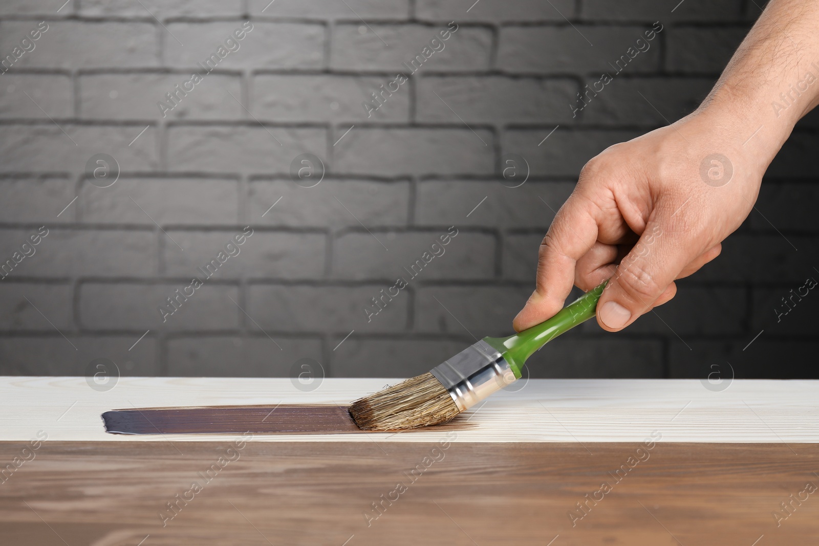 Photo of Man with brush applying walnut wood stain onto wooden surface, closeup