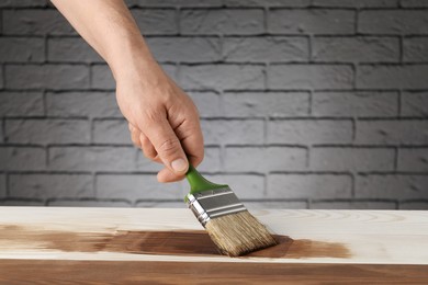 Photo of Man with brush applying walnut wood stain onto wooden surface, closeup