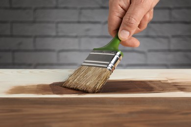 Photo of Man with brush applying walnut wood stain onto wooden surface, closeup