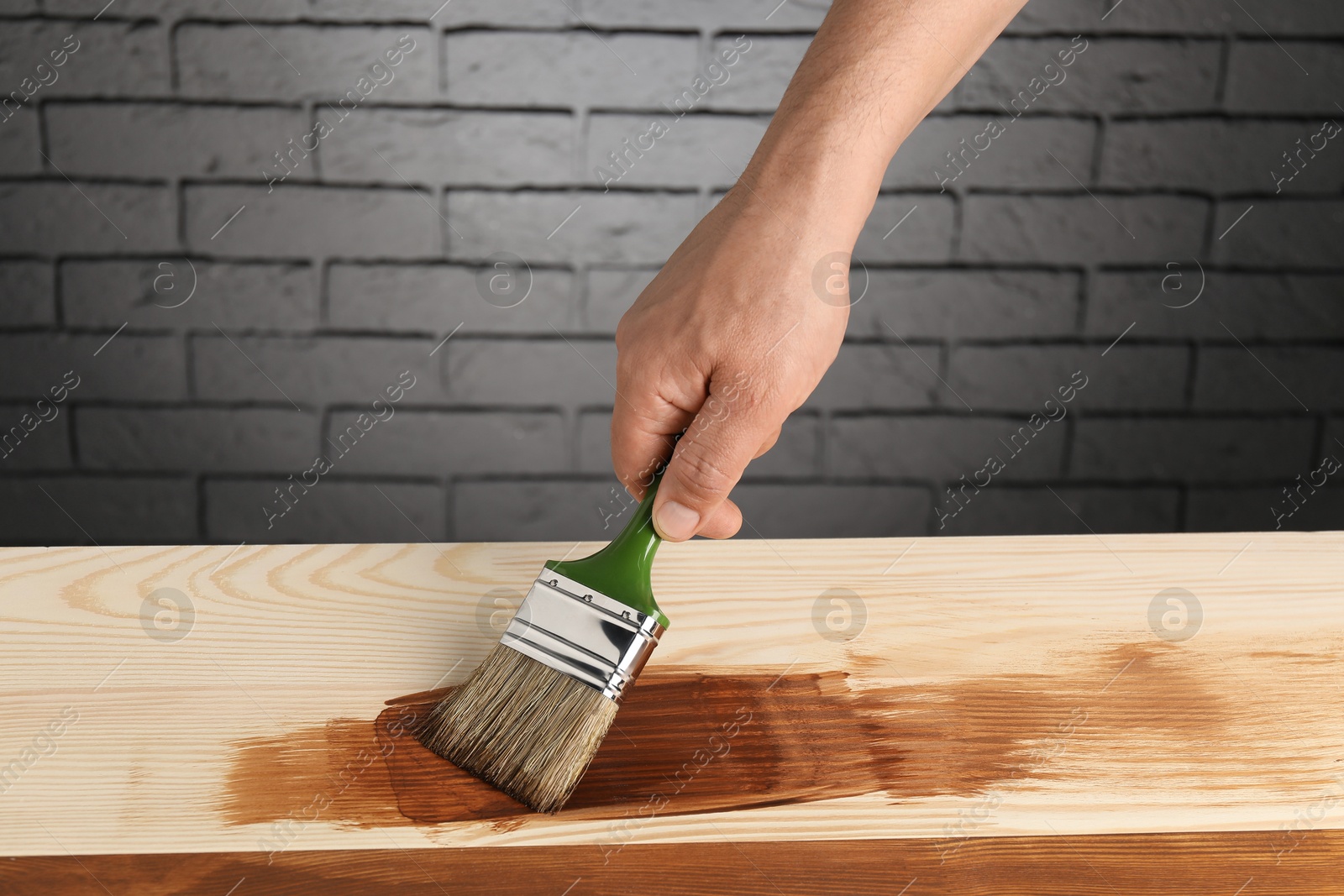 Photo of Man with brush applying walnut wood stain onto wooden surface, closeup