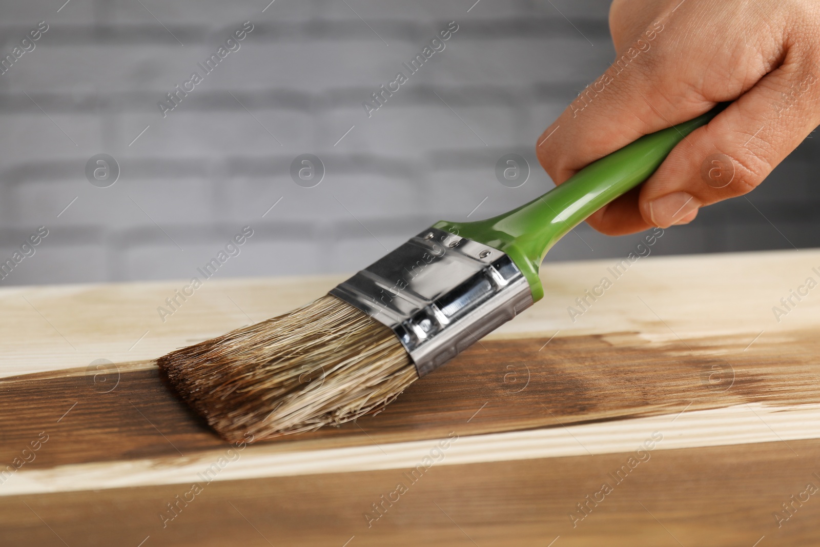 Photo of Man with brush applying walnut wood stain onto wooden surface, closeup