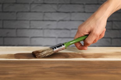 Photo of Woman with brush applying walnut wood stain onto wooden surface, closeup