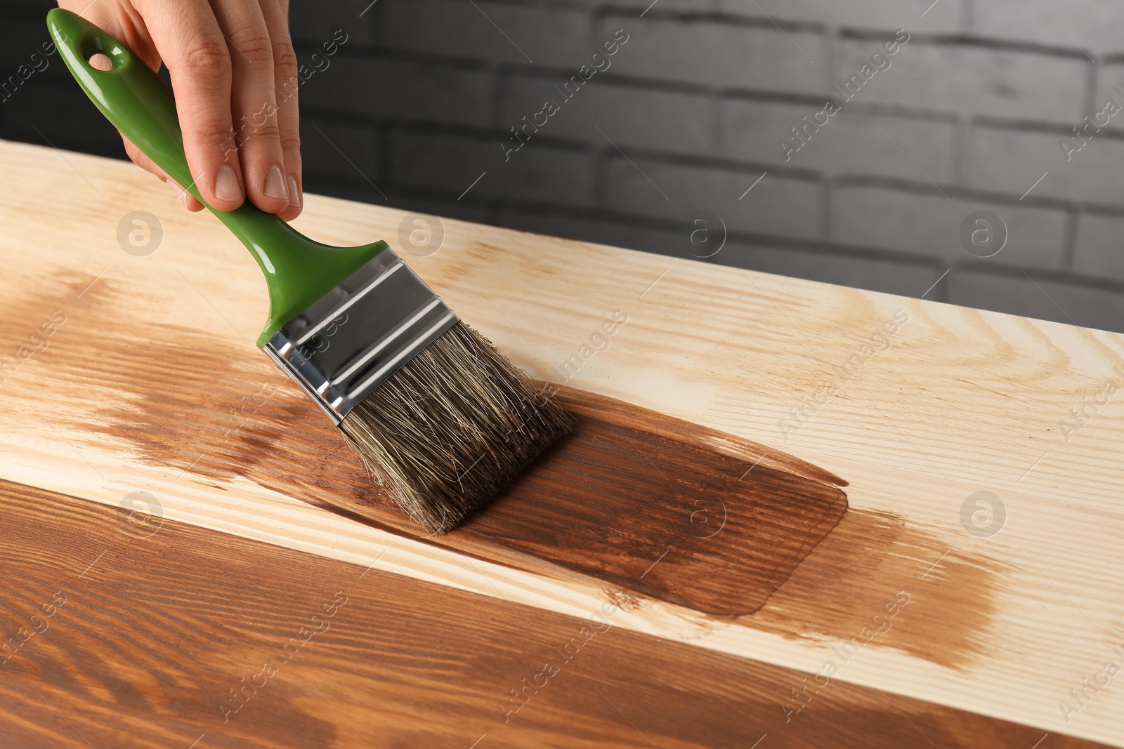 Photo of Woman with brush applying walnut wood stain onto wooden surface, closeup