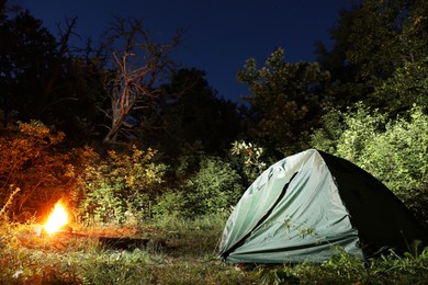 Bonfire and camping tent in forest at night