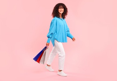 Smiling woman with colorful shopping bags on pink background