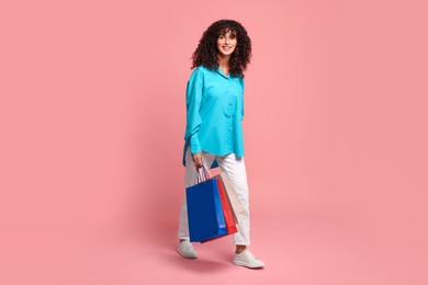 Smiling woman with colorful shopping bags on pink background