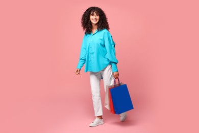 Smiling woman with colorful shopping bags on pink background