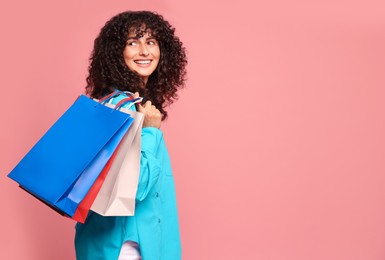 Smiling woman with colorful shopping bags on pink background. Space for text