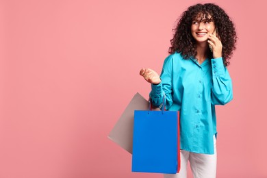 Photo of Smiling woman with colorful shopping bags talking by smartphone on pink background. Space for text