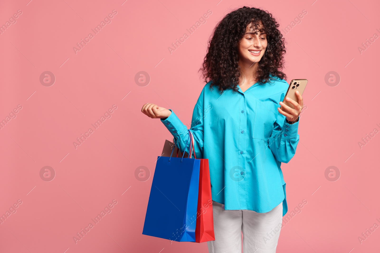 Photo of Smiling woman with colorful shopping bags and smartphone on pink background. Space for text