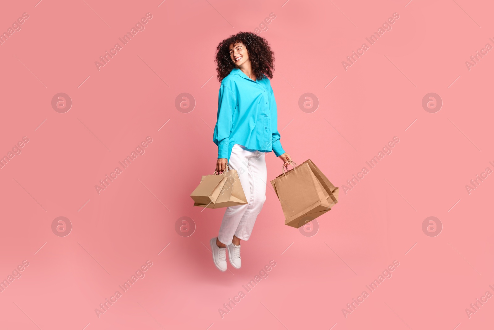 Photo of Smiling woman jumping with shopping bags on pink background