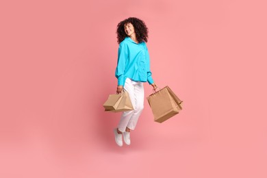 Smiling woman jumping with shopping bags on pink background