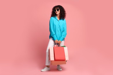 Smiling woman with colorful shopping bags on pink background