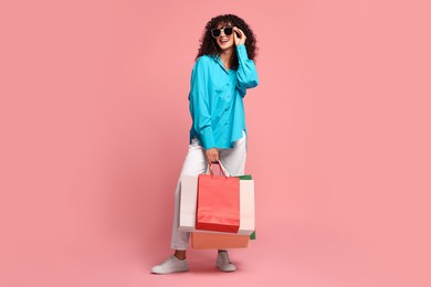 Smiling woman with colorful shopping bags on pink background