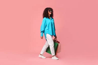 Smiling woman with colorful shopping bags on pink background