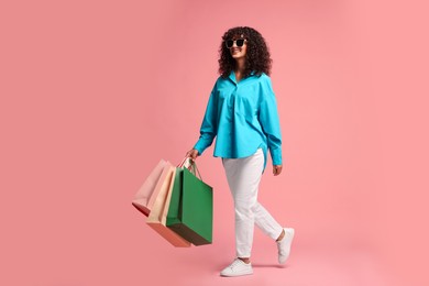 Smiling woman with colorful shopping bags on pink background