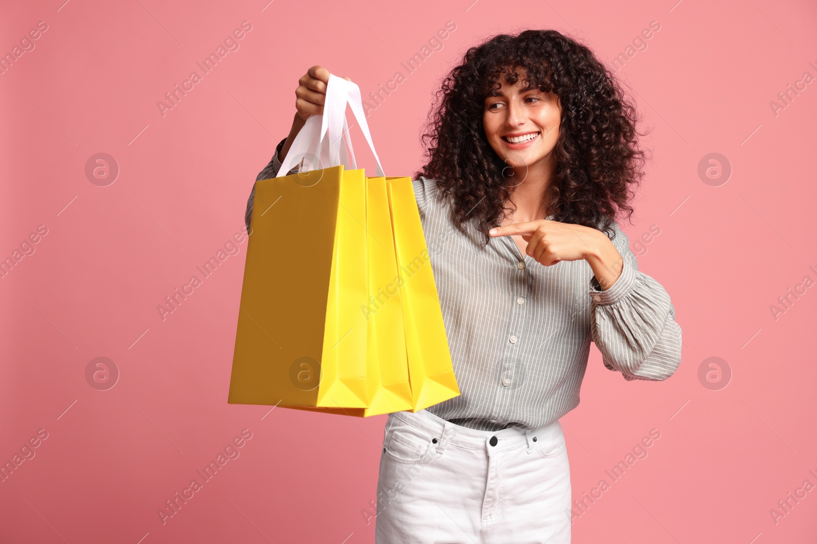 Photo of Smiling woman pointing at shopping bags on pink background