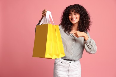 Smiling woman pointing at shopping bags on pink background